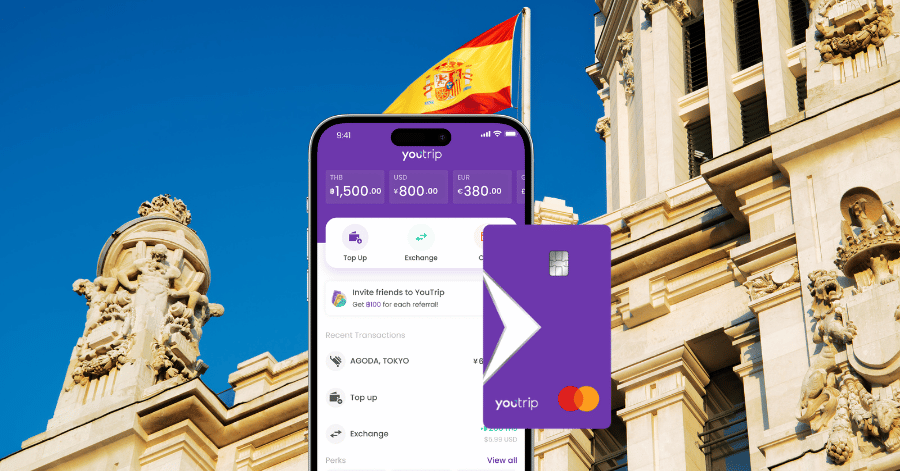 YouTrip app and purple card held in front of a Spanish flag and palace facade