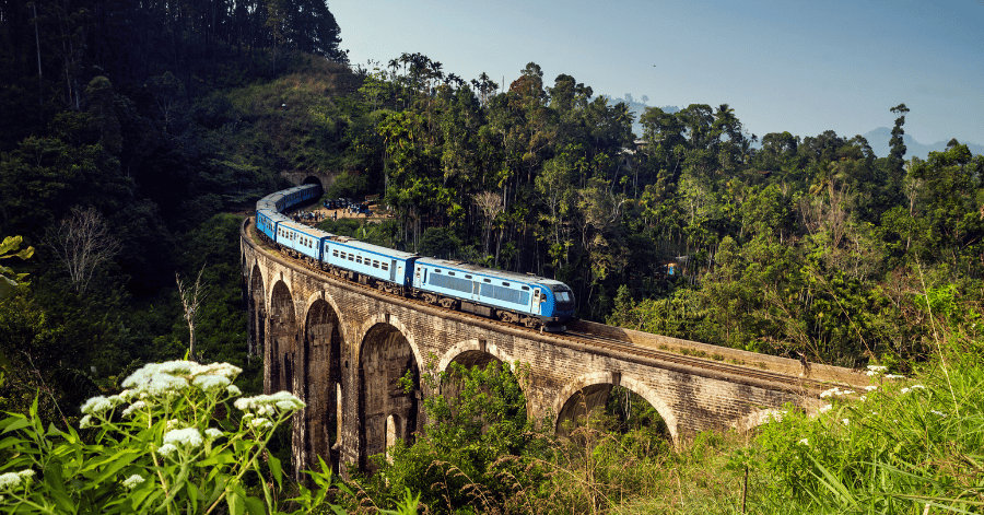A blue train crossing the Nine Arch Bridge through lush jungle near Ella, Sri Lanka