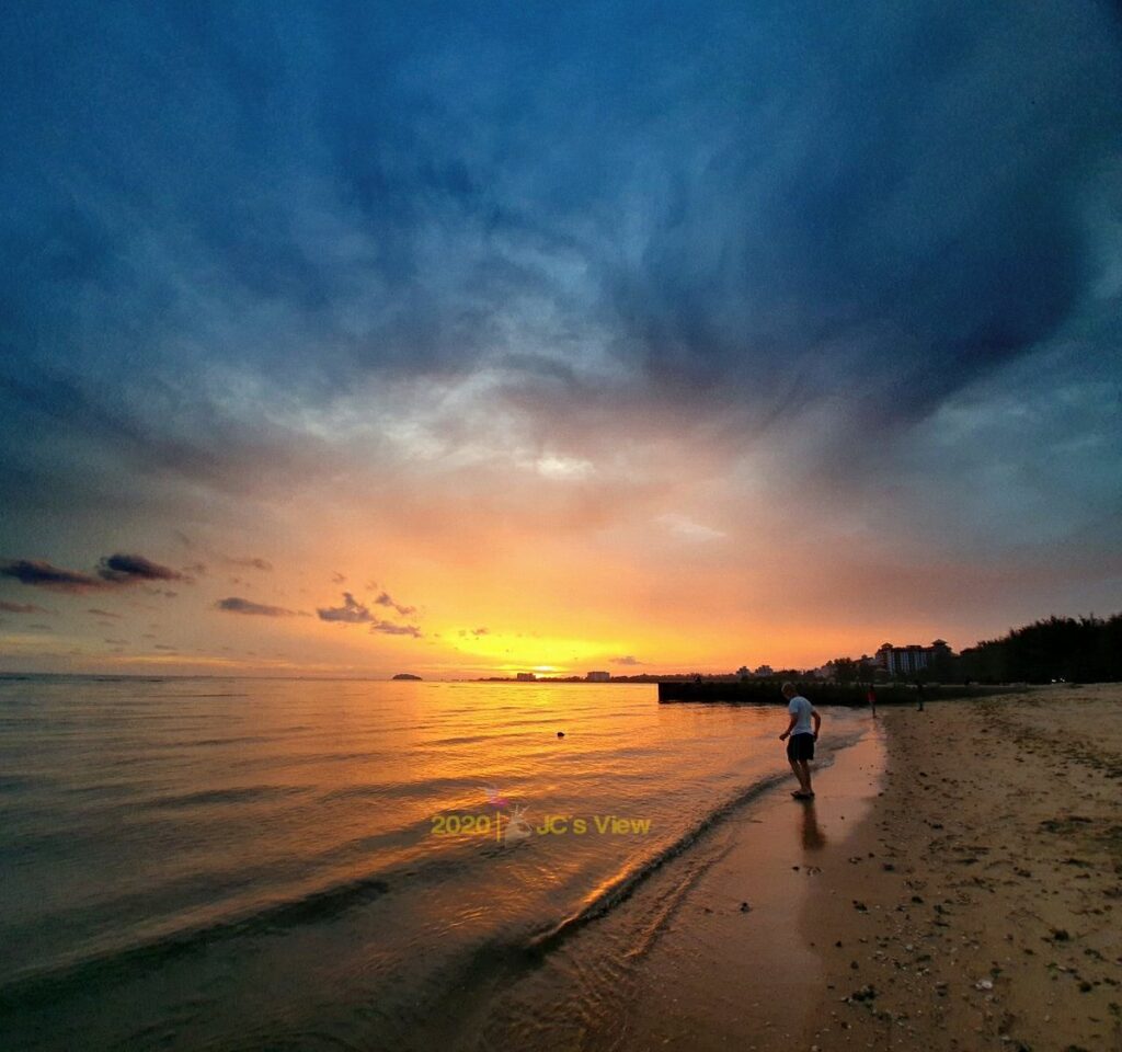 Dramatic orange sunset over the sea with a person walking along the shoreline