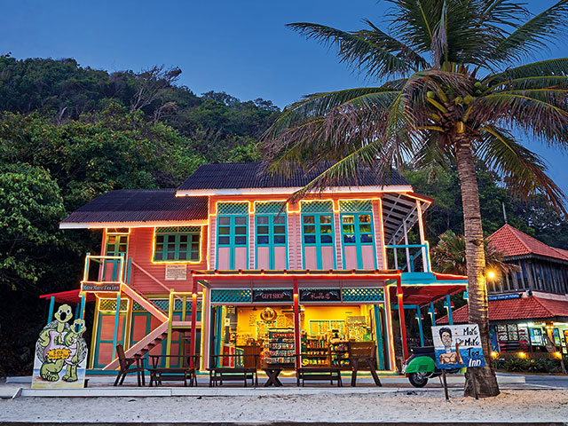 Brightly painted two-storey More More Tea Inn gift shop lit up at dusk by the beach
