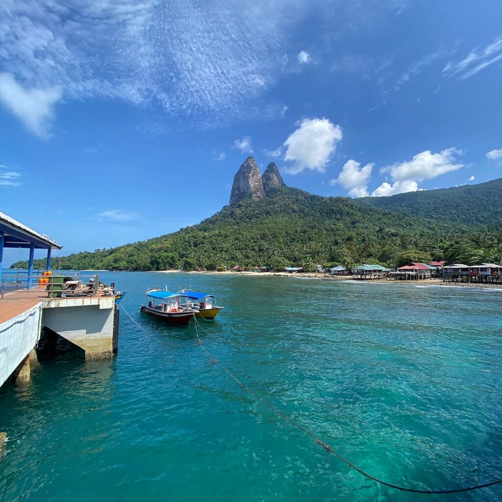 The twin Dragon's Horns peaks rising behind Mukut village, boats and a jetty on Tioman