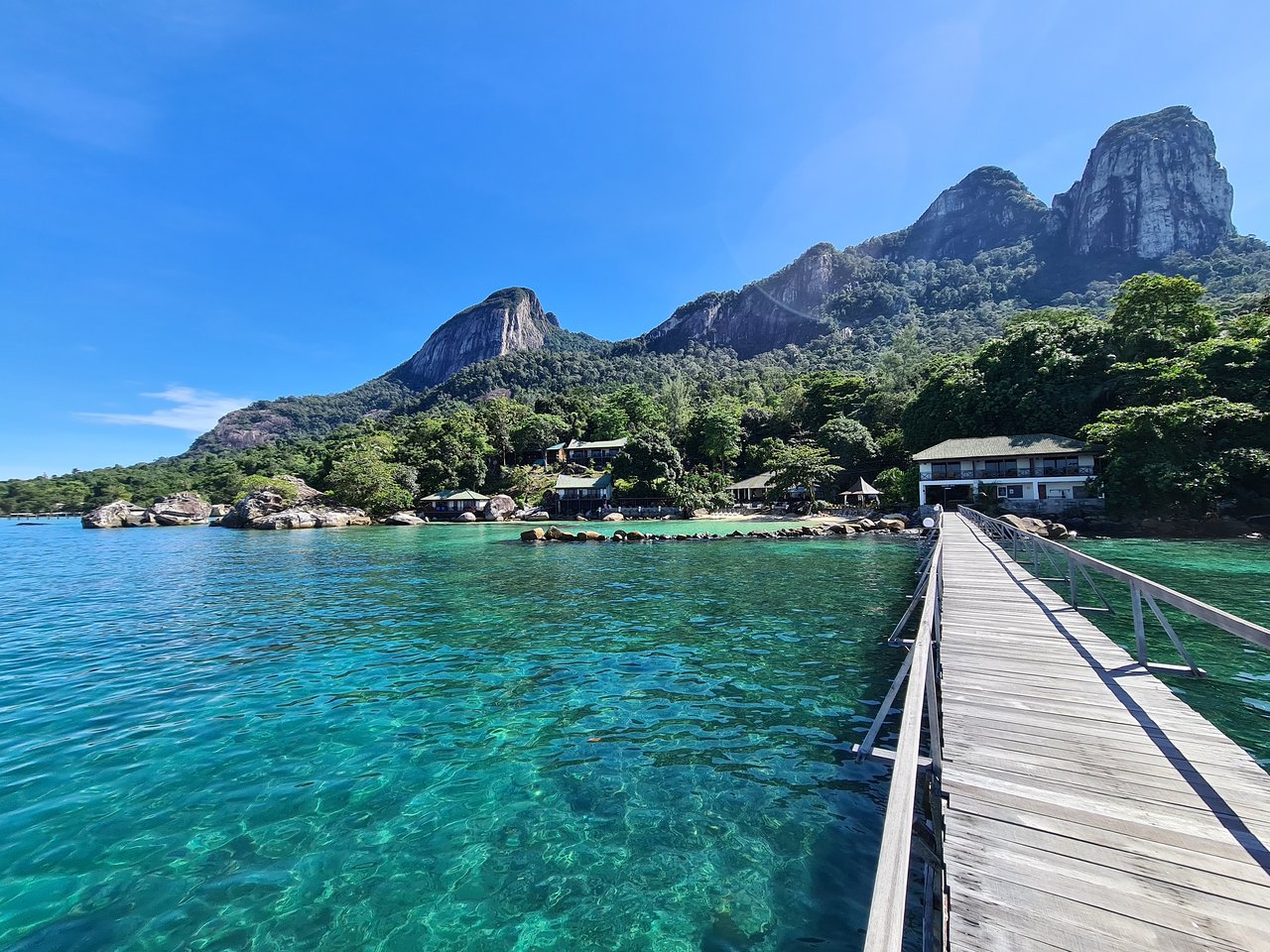 A wooden jetty stretching over clear turquoise water toward jungle peaks on Tioman
