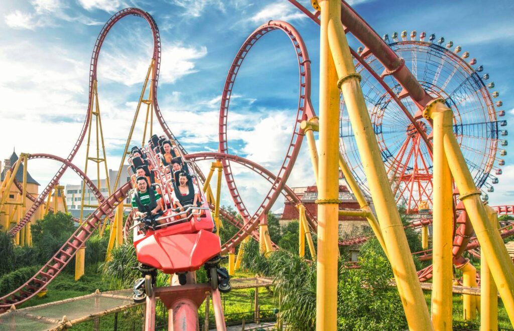 Riders on a looping roller coaster beside a Ferris wheel at VinWonders Phu Quoc
