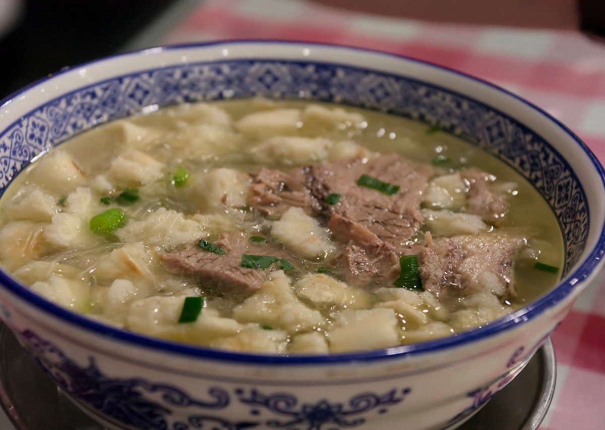 A bowl of yangrou paomo, lamb soup with torn flatbread and spring onion