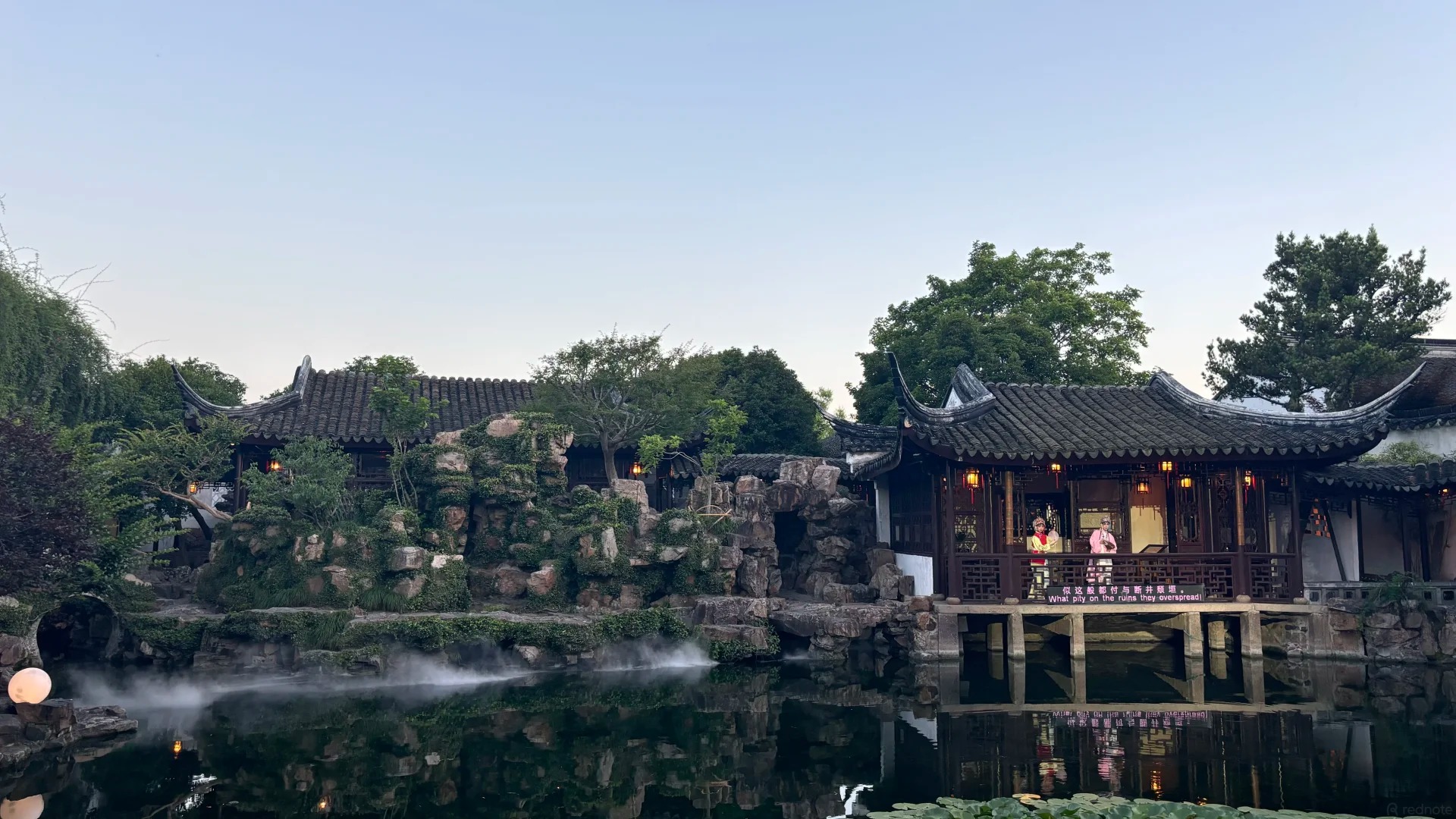 A lamplit garden pavilion and misty pond at dusk during the Master of the Nets night show