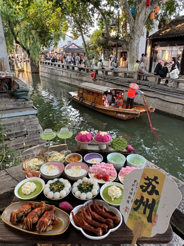 A spread of Suzhou snacks, crab and rice balls on a ledge above a canal with a boat