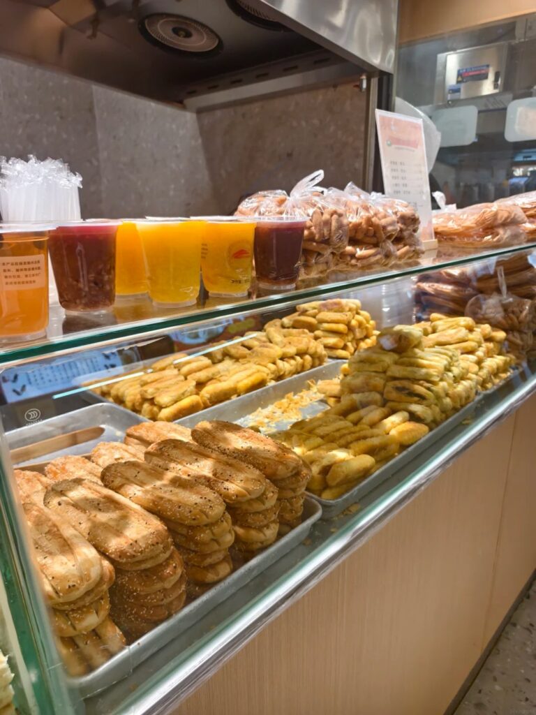 Trays of fried local snacks and cups of drinks in a Suzhou market display case