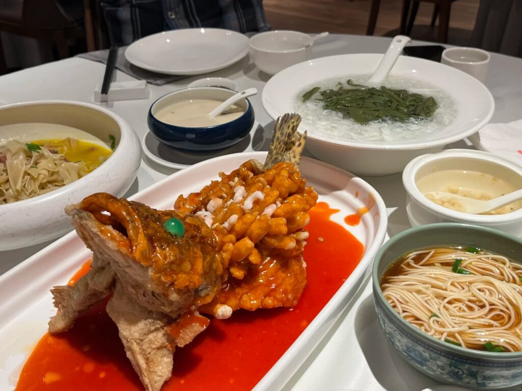 Squirrel-shaped mandarin fish in red sauce beside a bowl of clear-broth Suzhou noodles