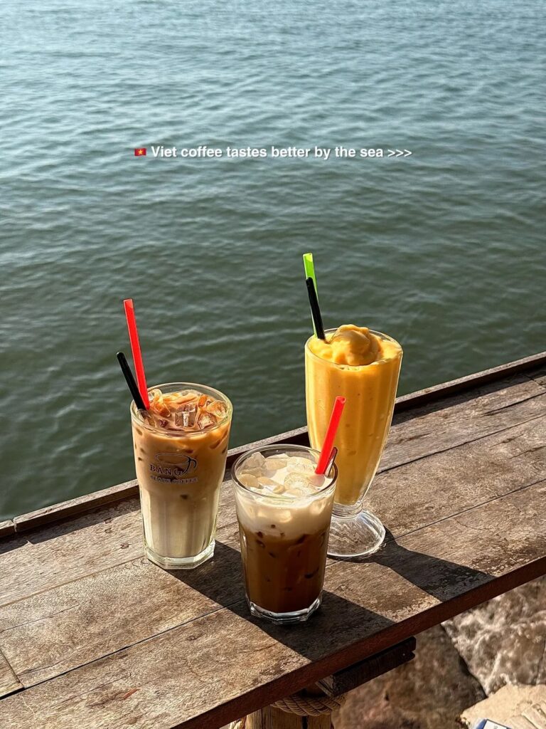 Three iced Vietnamese coffees on a wooden ledge overlooking the sea at a Phu Quoc cafe