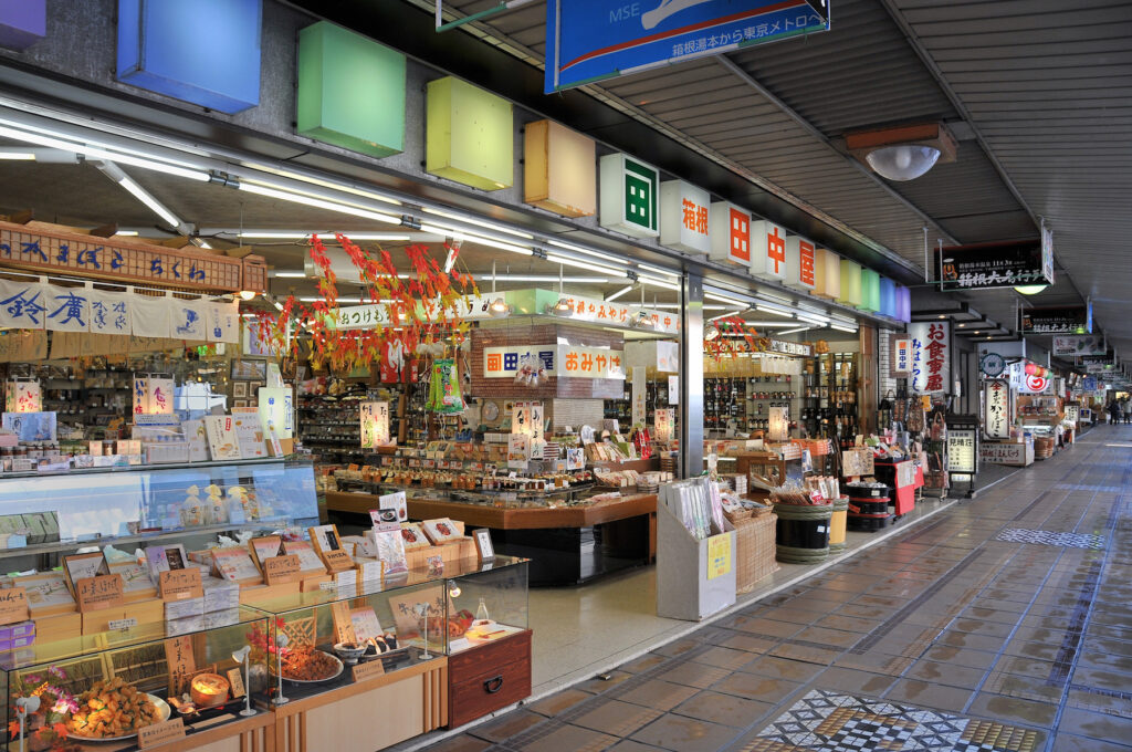 A covered arcade of souvenir and snack shops with glass display cases at Hakone-Yumoto