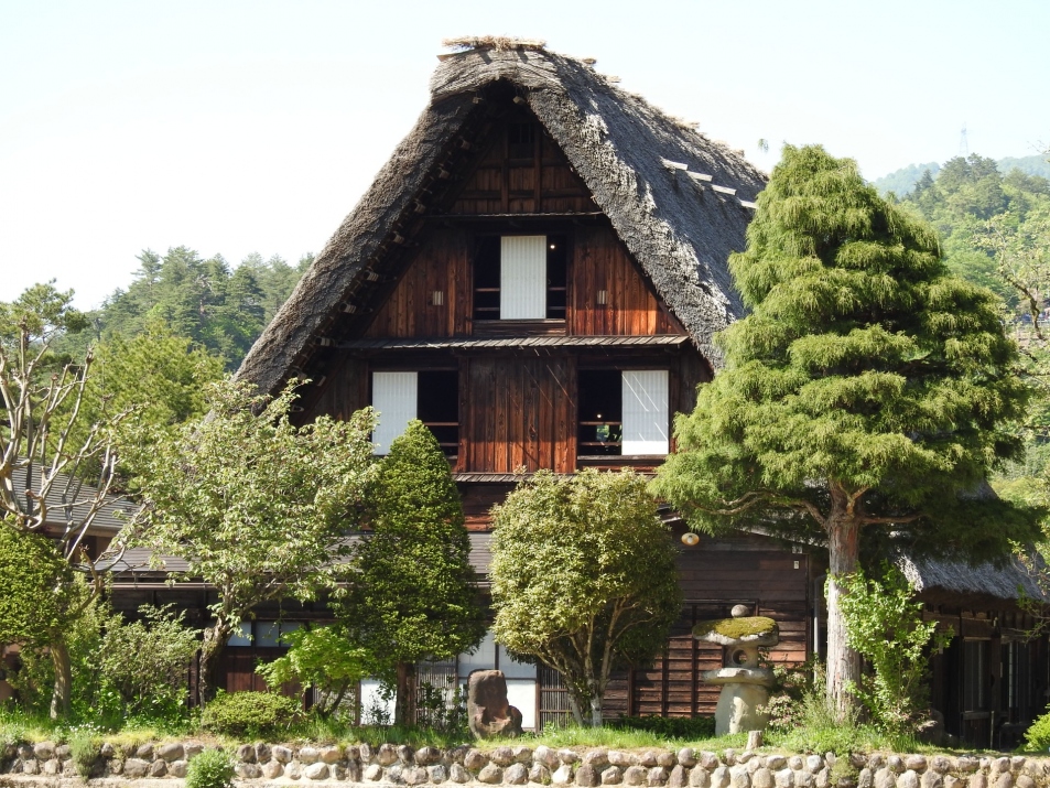 A large thatched-roof gassho-zukuri farmhouse behind a garden and stone base
