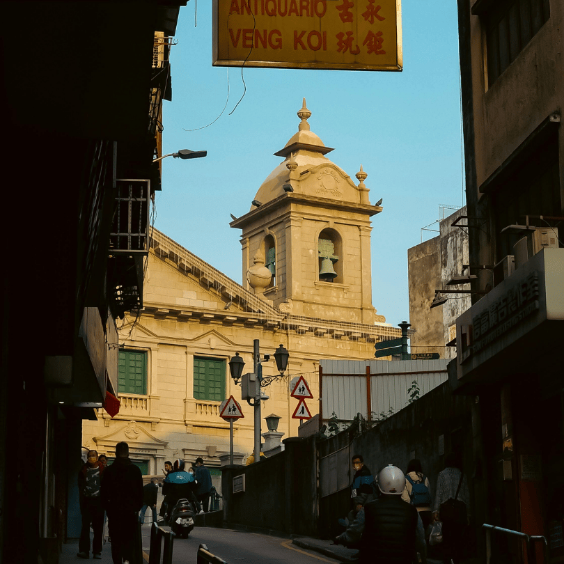 A colonial-era church bell tower rising above a Macau side street at golden hour