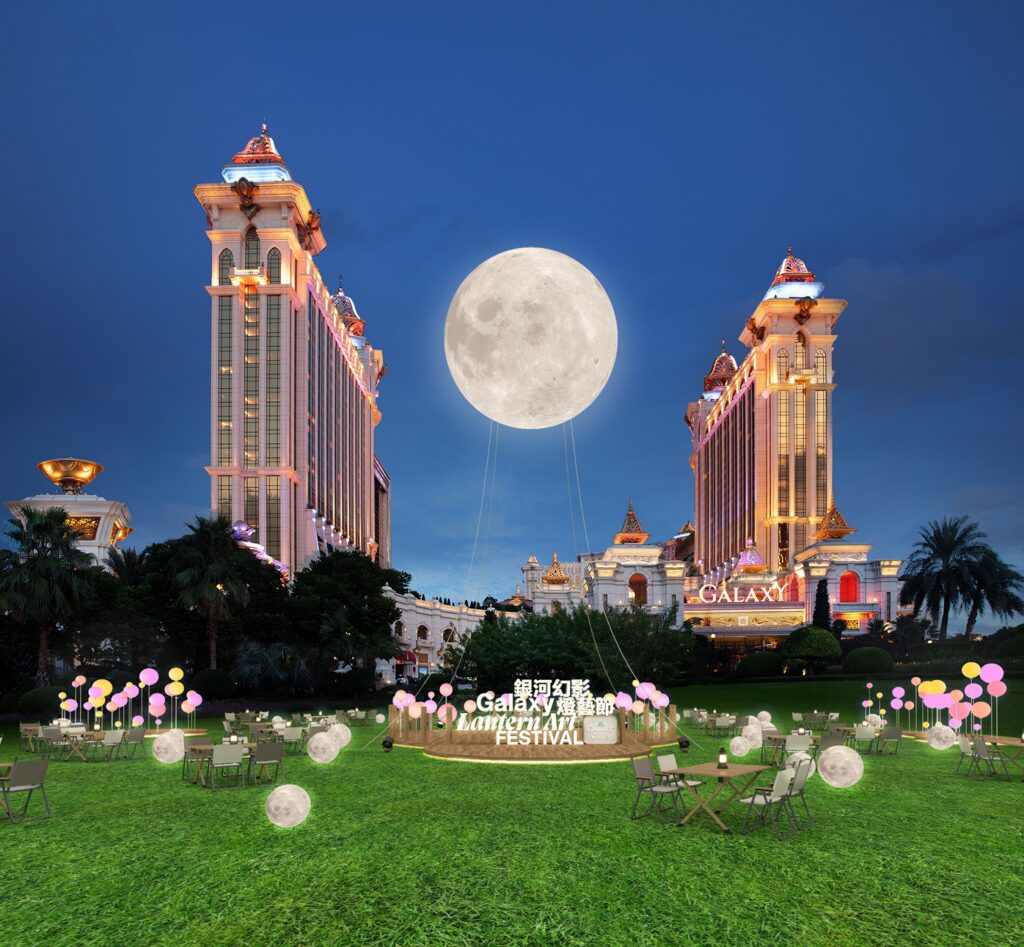 Galaxy Macau's golden towers at dusk behind a giant illuminated moon and lantern-festival lawn