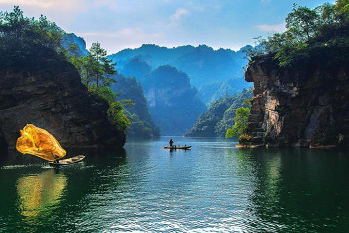 A fisherman casting a golden net from a boat on Baofeng Lake between forested peaks