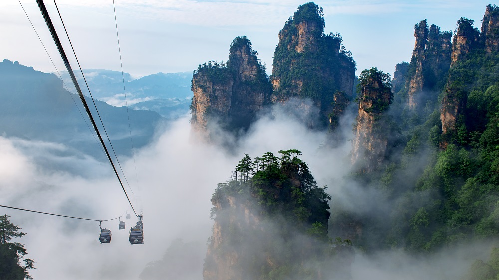 Cable-car gondolas rising past mist-wrapped sandstone pillars at Yangjiajie