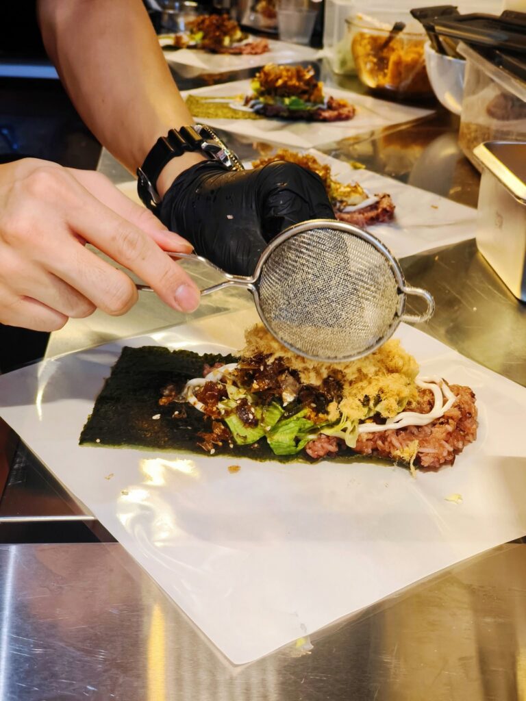 A stall hand-making a seaweed-wrapped rice roll, dusting it with pork floss, at Chun Man Ren Jian