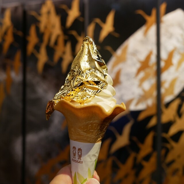 A soft-serve ice cream cone wrapped in a full sheet of gold leaf, held up in Kanazawa