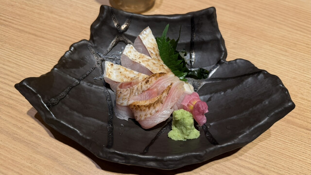 Lightly seared nodoguro (blackthroat seaperch) sashimi on a black plate with wasabi