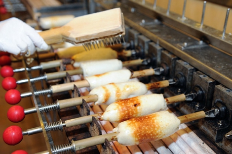 White fish-paste chikuwa rolls being grilled on bamboo skewers on a production line