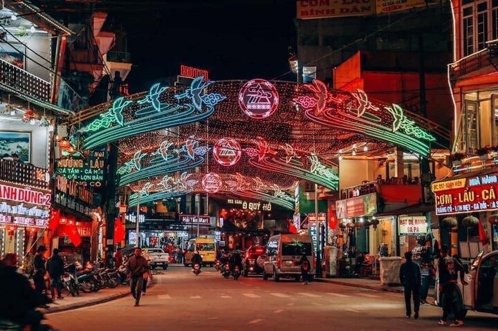 A Sapa town street lit with neon arches at night, lined with hotpot and salmon restaurants and shops