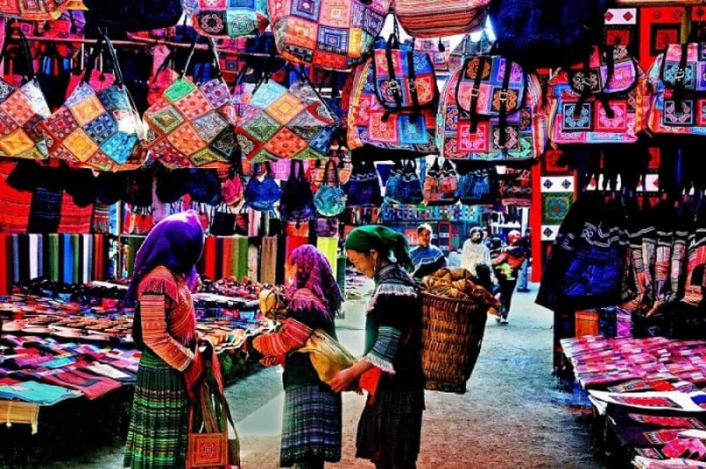 Flower H'mong women browsing stalls hung with colourful embroidered bags and textiles at Bac Ha market
