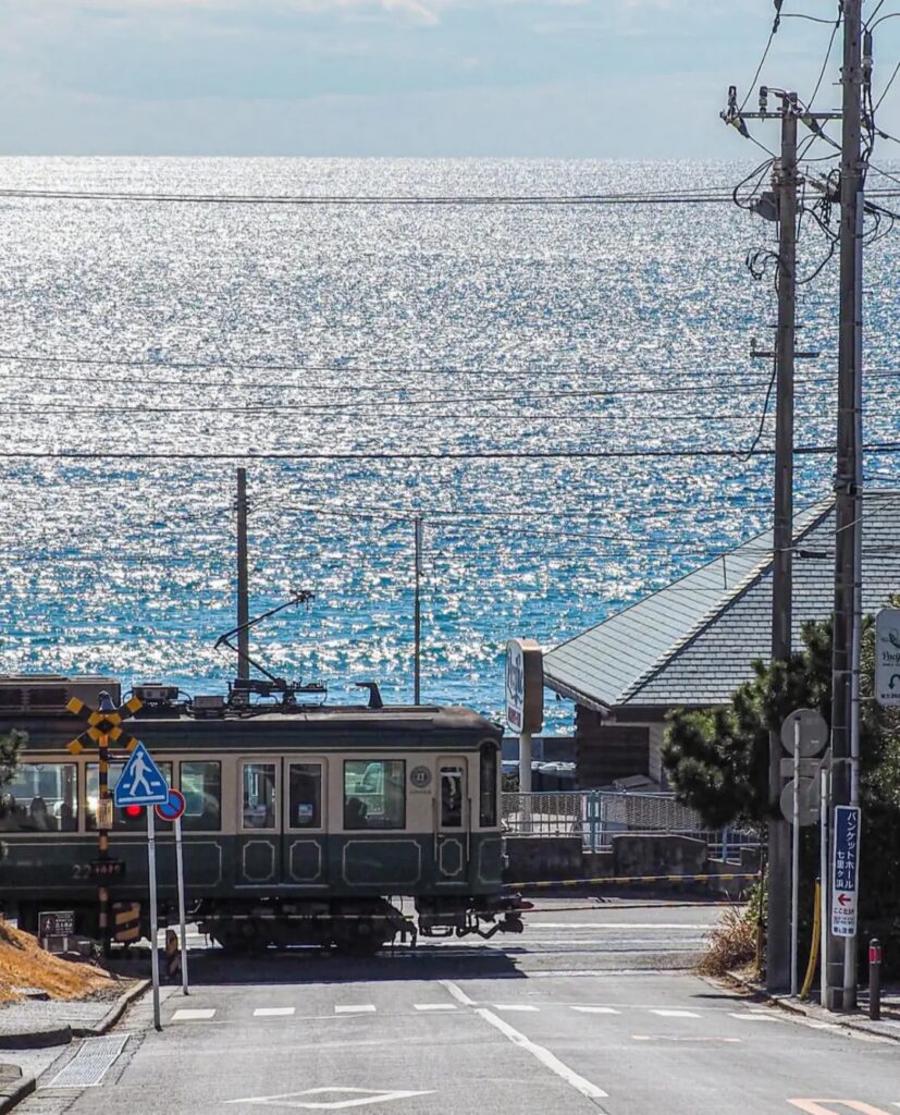 The green Enoden train at a seaside railway crossing with the sparkling sea behind, Kamakura