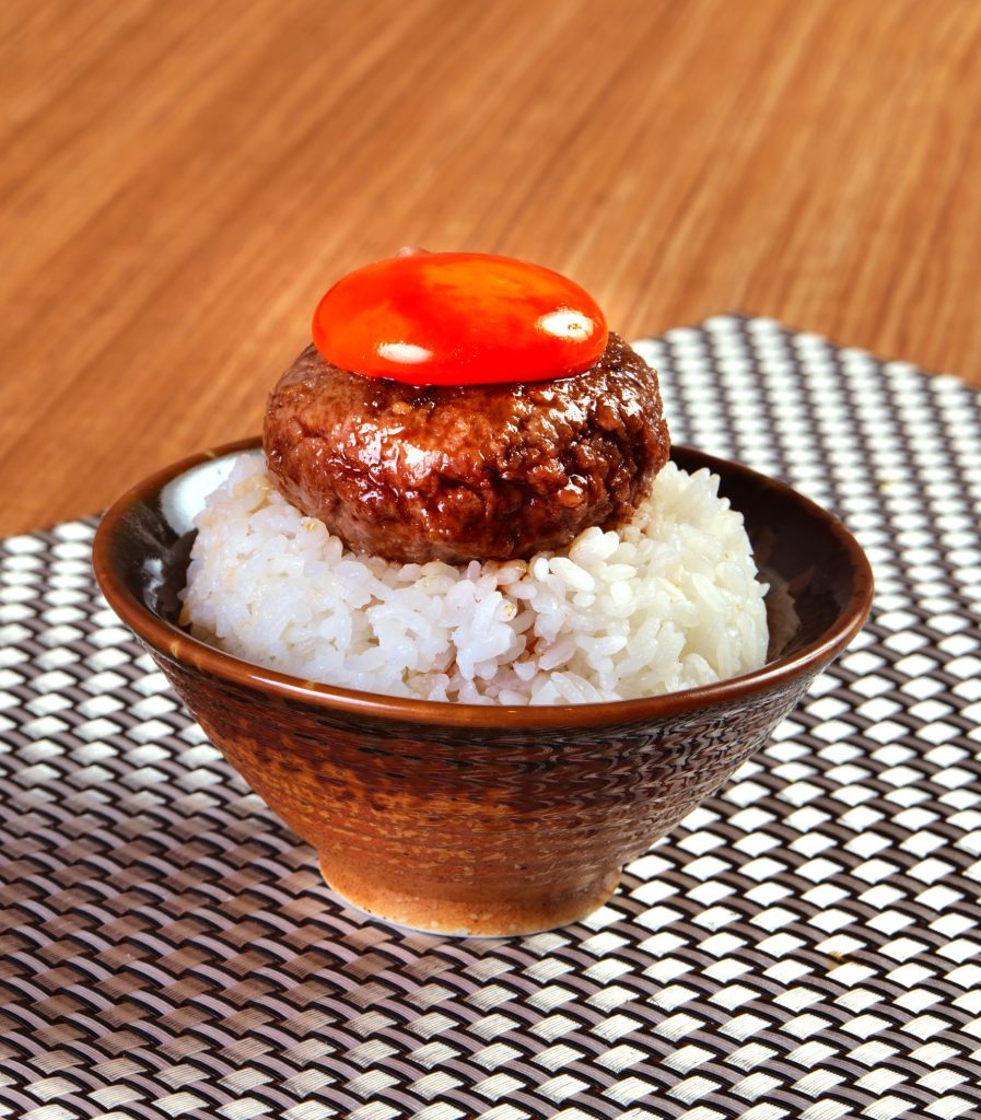 Wagyu hamburg steak topped with a soft egg yolk over a bowl of white rice