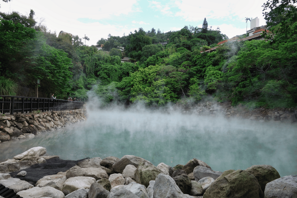 Steam rising from a turquoise geothermal hot-spring pool surrounded by forest in Beitou, Taipei