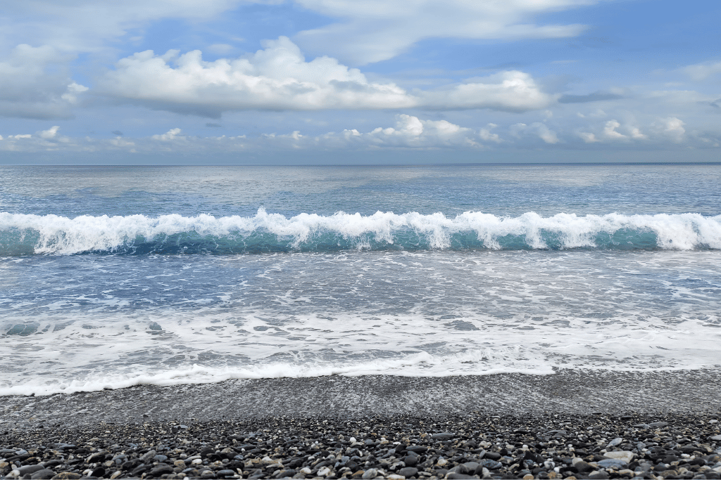 Waves breaking on a grey pebble beach under a cloudy blue sky on Taiwan's coast