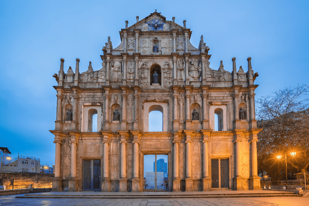 The stone facade of the Ruins of St. Paul's lit at dusk against a blue sky in Macau