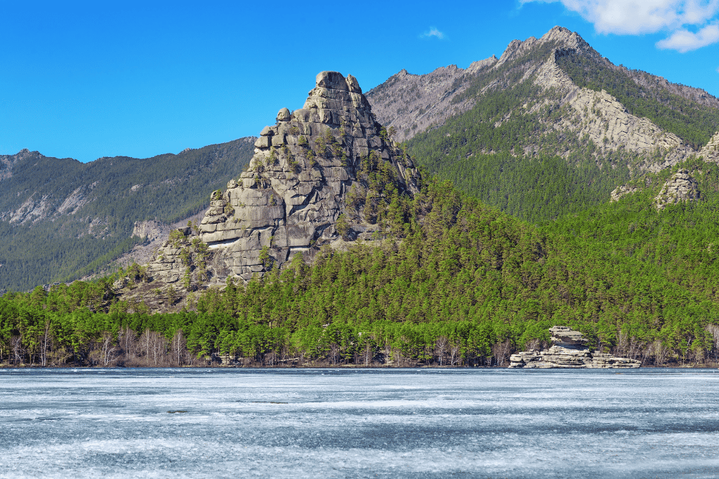 A rocky granite outcrop above a frozen lake and pine forest in Burabay
