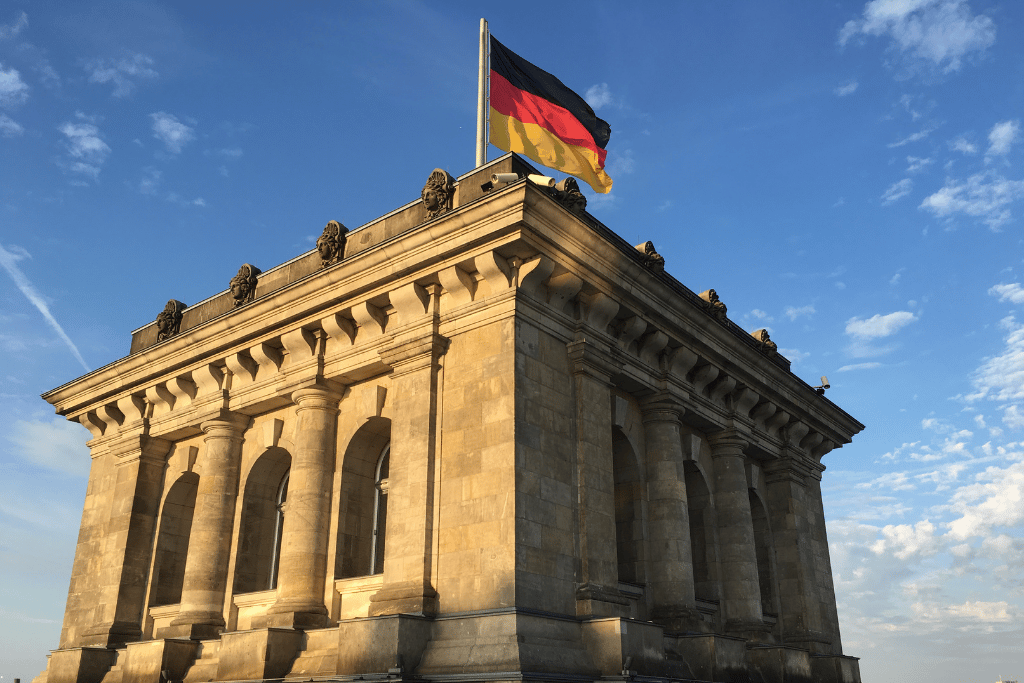 The German flag flying above the stone Reichstag building in Berlin against a blue sky