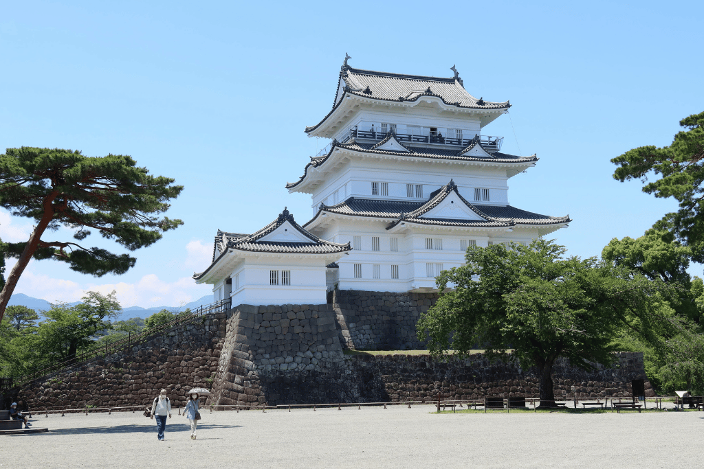 The white multi-tiered keep of Odawara Castle on its stone base under a blue sky