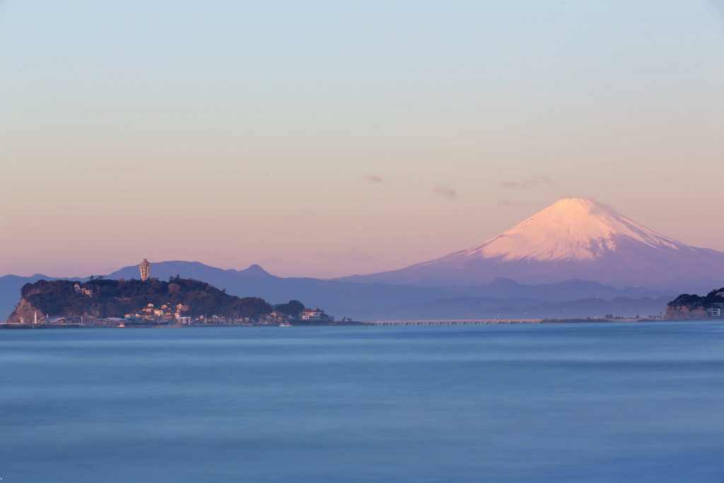 Enoshima island with its observation tower and Mt Fuji behind at dusk across the bay