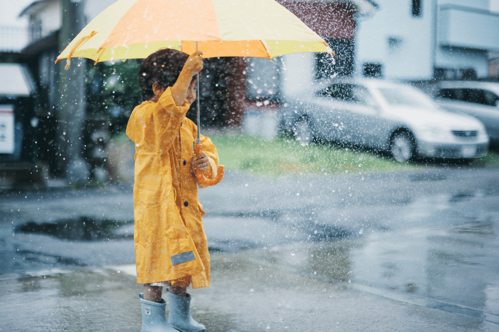 A child in a yellow raincoat holds an umbrella in the rain on a wet street in Taiwan