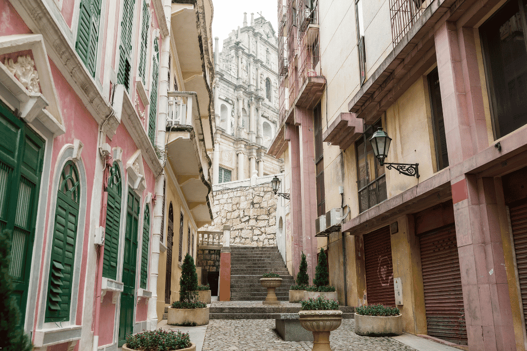 A narrow pastel-toned Macau lane with green shutters leading up to the Ruins of St. Paul's