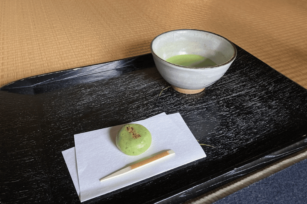 A bowl of matcha and a green wagashi sweet on a black tray on tatami
