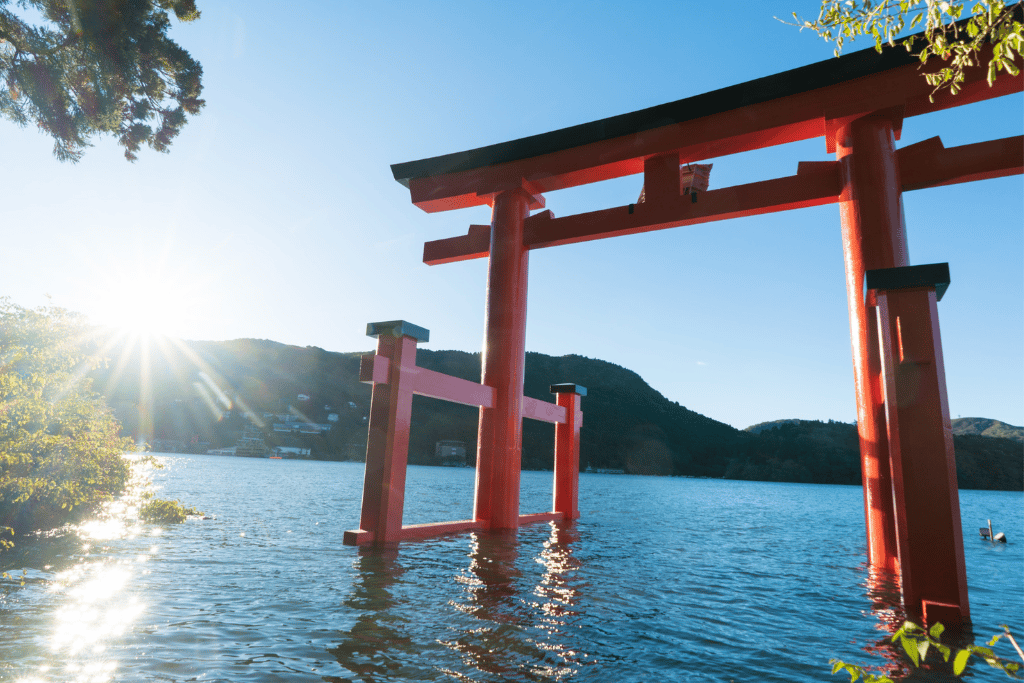The red Peace Torii of Hakone Shrine standing in the water of Lake Ashi, backlit by the sun