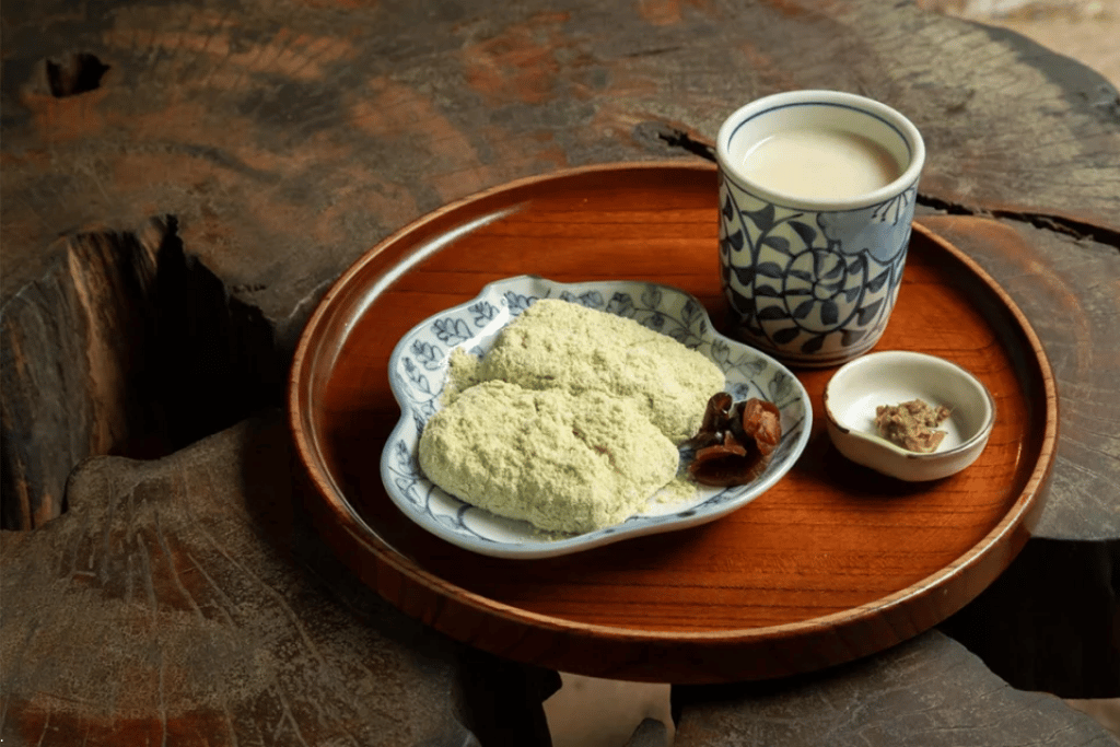 A plate of soybean-dusted mochi and a cup of amazake on a wooden tray