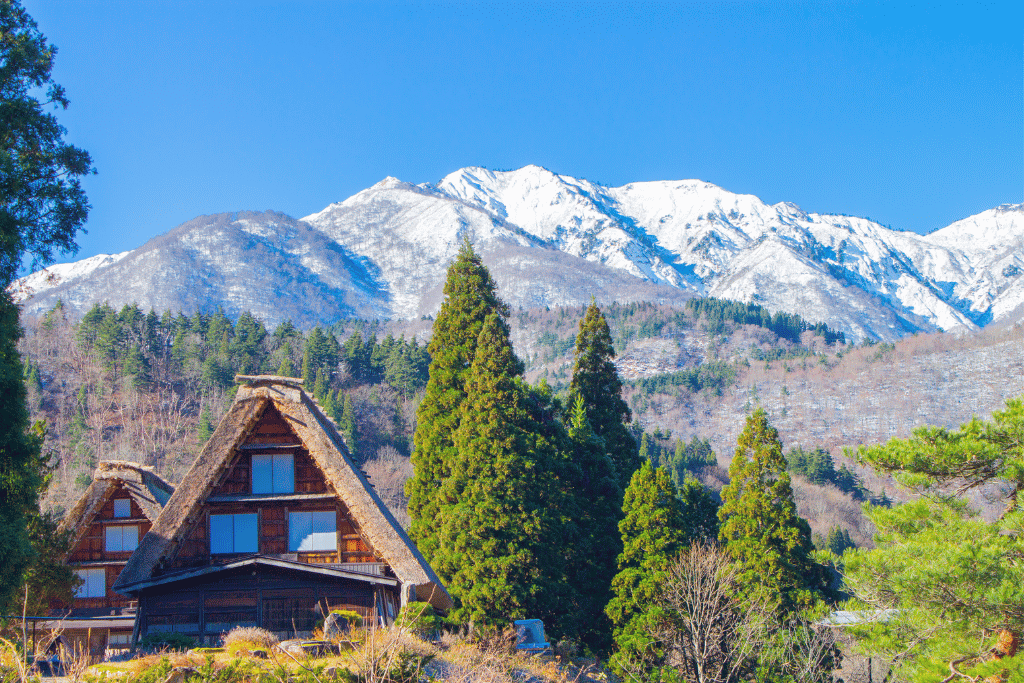A thatched gassho-zukuri farmhouse in Shirakawago below snow-capped peaks under a clear blue sky