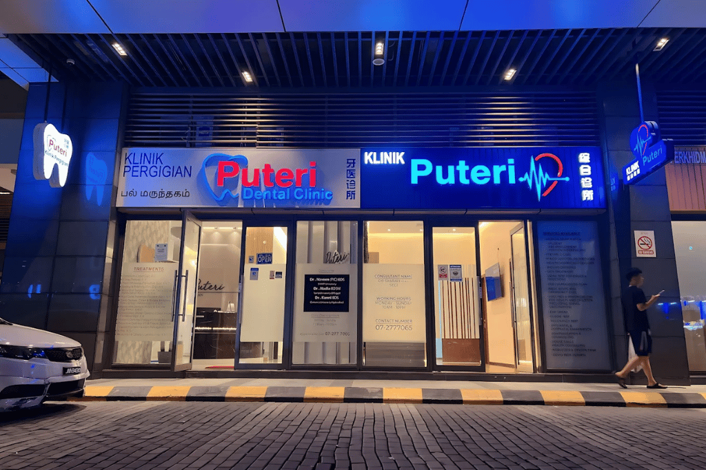 Puteri Dental Clinic's lit blue shopfront at R&F Mall in the evening, with a passer-by walking past