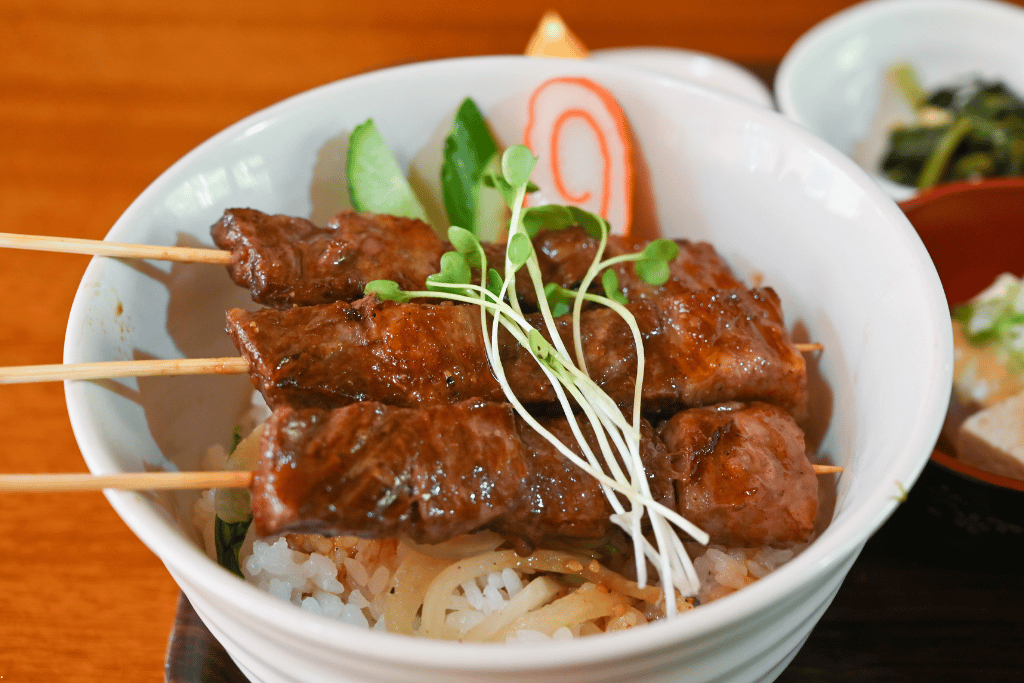A rice bowl topped with three grilled Hida beef skewers and microgreens