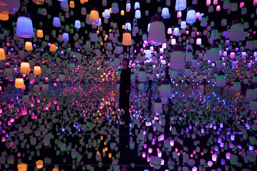 Person standing among hundreds of glowing hanging lamps in the Forest of Resonating Lamps