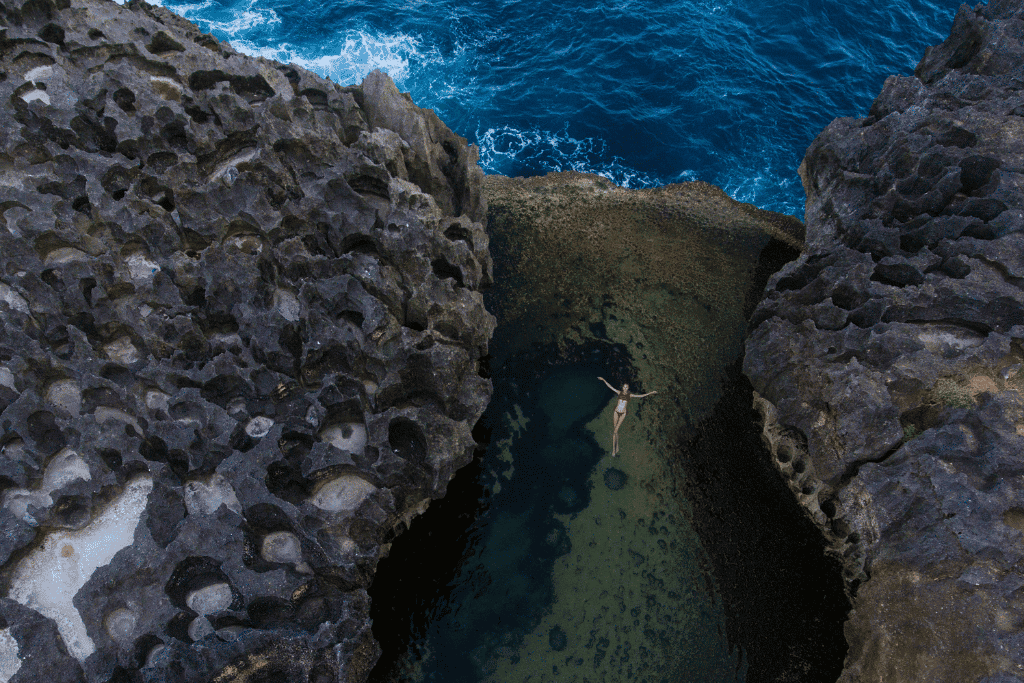 A swimmer floating in the natural tidal rock pool at Angel's Billabong, waves breaking beyond
