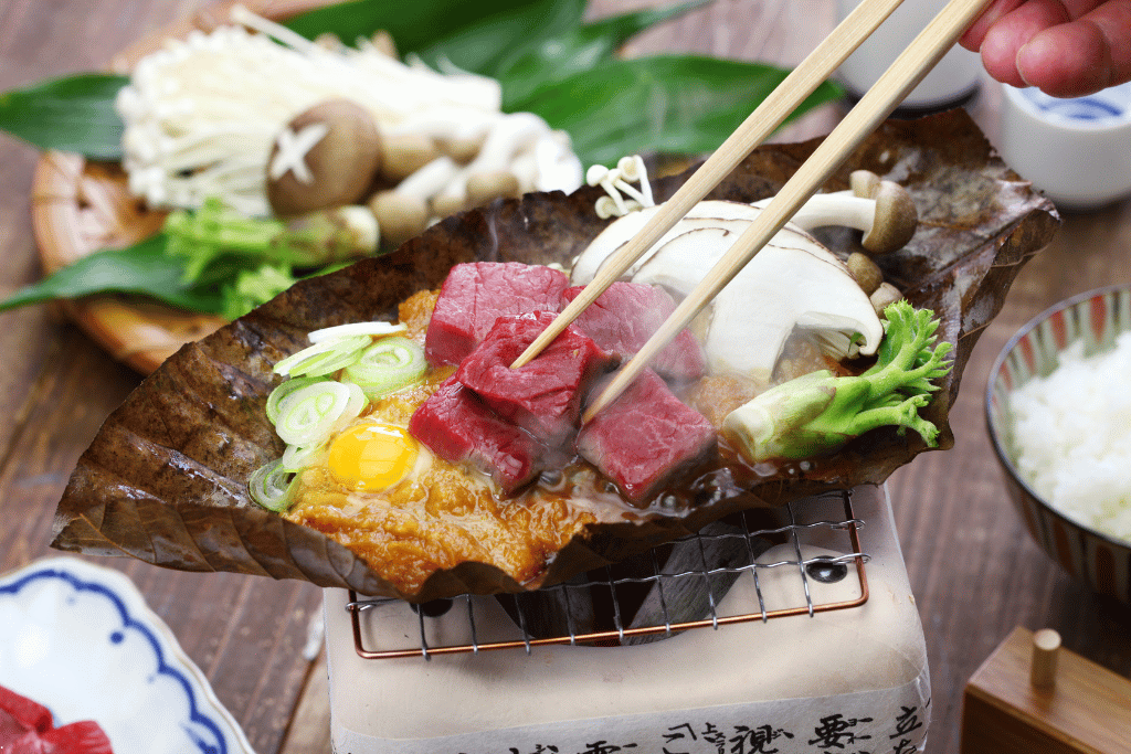 Hida beef, mushrooms and egg cooking on a dried magnolia leaf for hoba miso