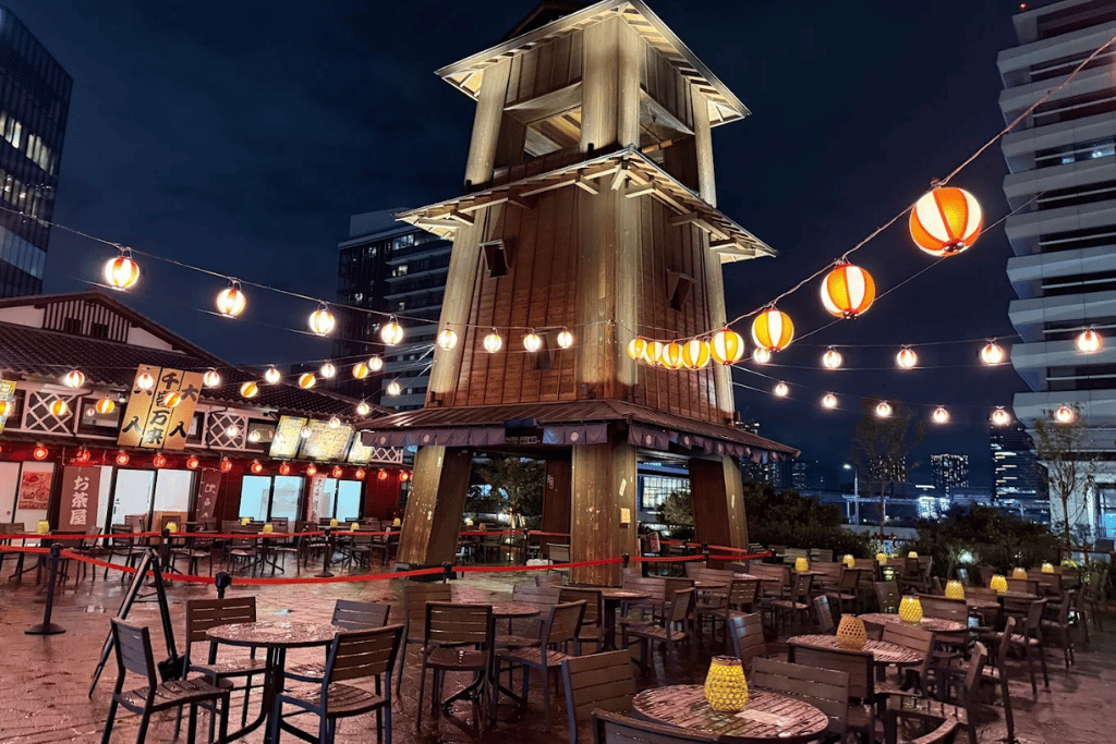 Edo-style wooden watchtower and paper lanterns above outdoor dining tables at Toyosu Senkyaku Banrai