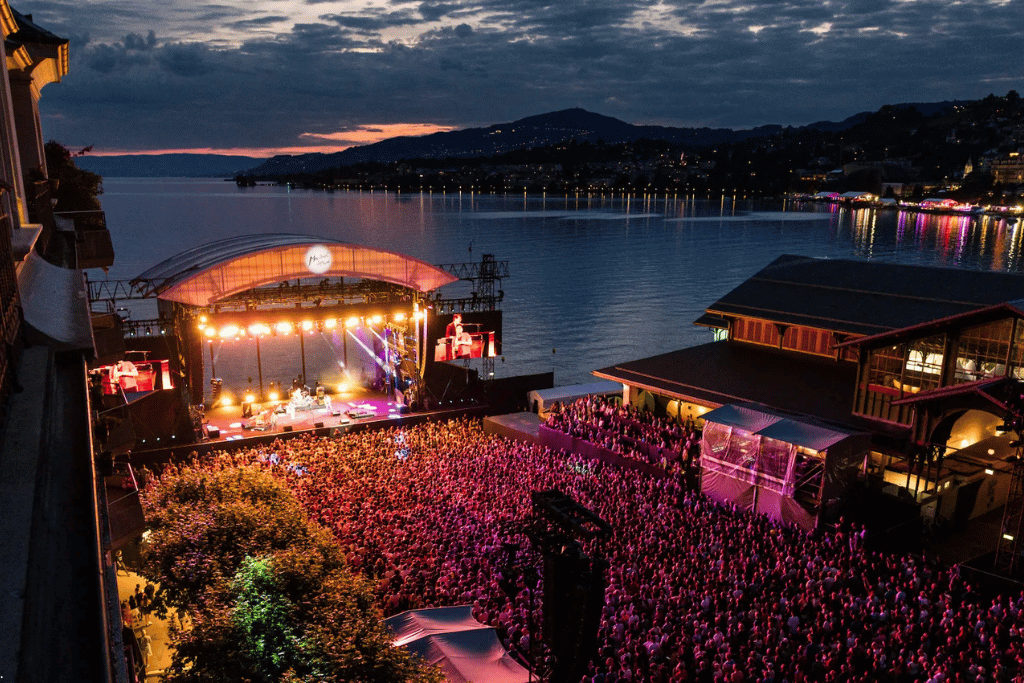 A large crowd at a lakeside concert stage at dusk during the Montreux Jazz Festival