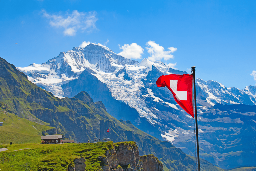 A Swiss flag flying on a green ridge before the snow-capped Jungfrau massif