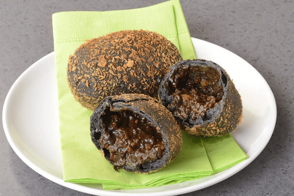 A black-crusted curry bread cut open to show the curry filling, on a plate