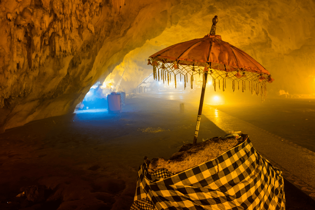 Inside the Goa Giri Putri cave temple, a Balinese ceremonial umbrella and checkered-cloth shrine